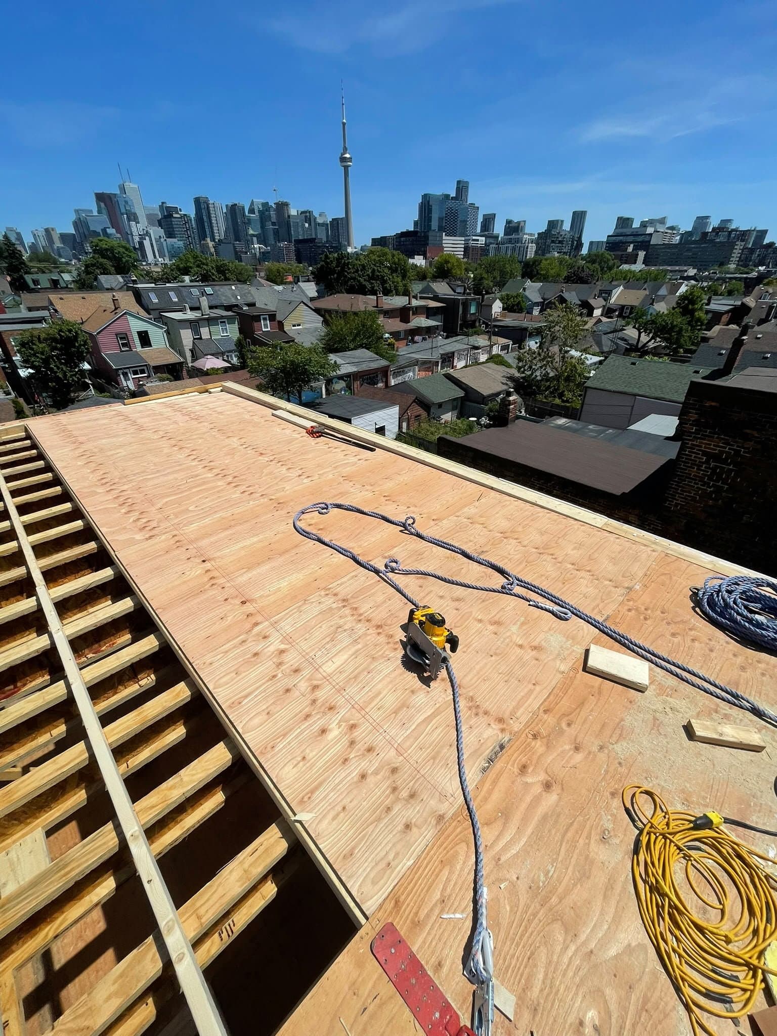 Rooftop framing and sheathing with the Toronto skyline and CN Tower in view
